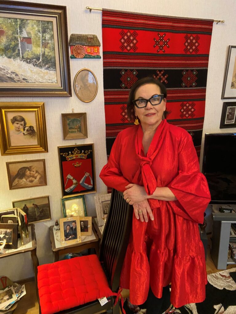 Nainen seisoo olohuoneessa, päällään punainen mekko